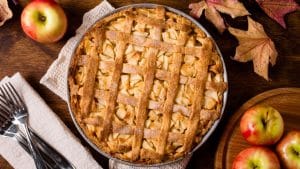 Torta de maçã com talheres, maçãs e folhas em volta.