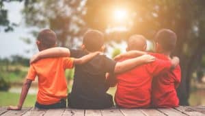 Crianças sentadas se costas se abraçando, representando as amizades.